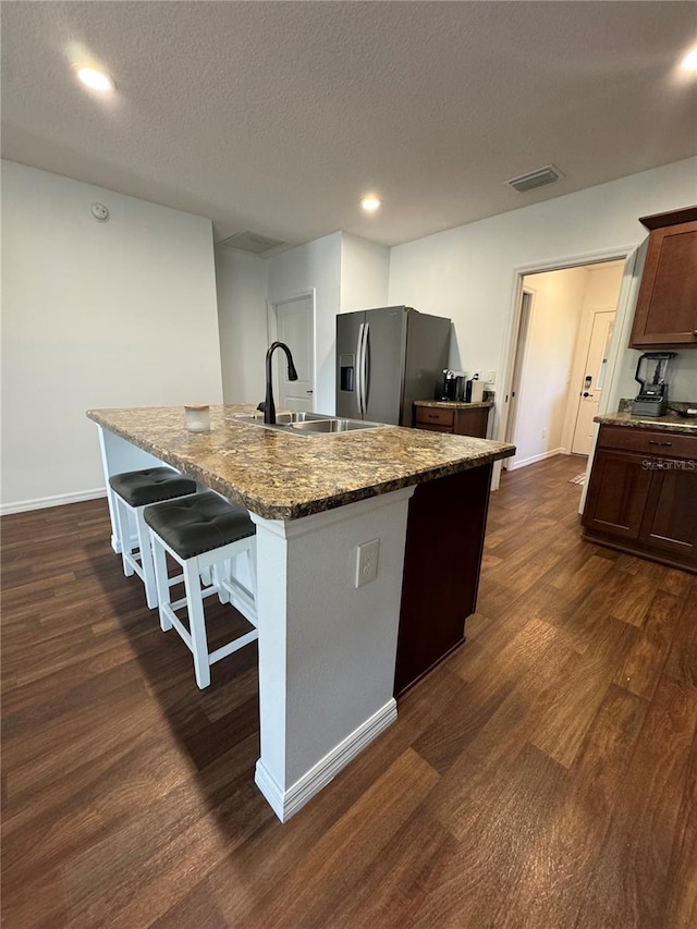 kitchen with a breakfast bar, sink, a center island with sink, dark hardwood / wood-style floors, and stainless steel fridge