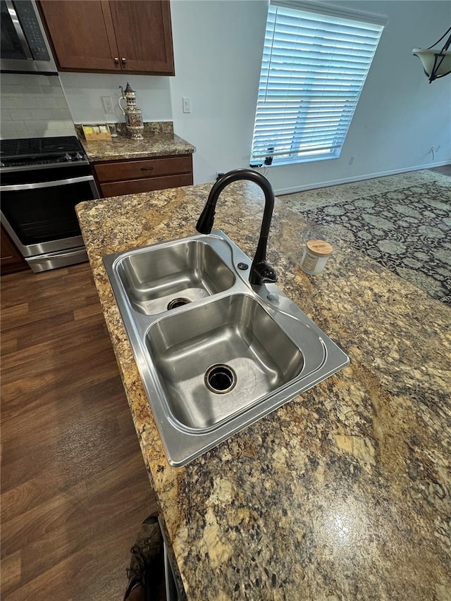 interior details featuring appliances with stainless steel finishes, sink, dark hardwood / wood-style flooring, dark stone counters, and dark brown cabinets