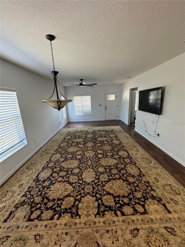 unfurnished living room featuring a textured ceiling, dark wood-type flooring, and ceiling fan