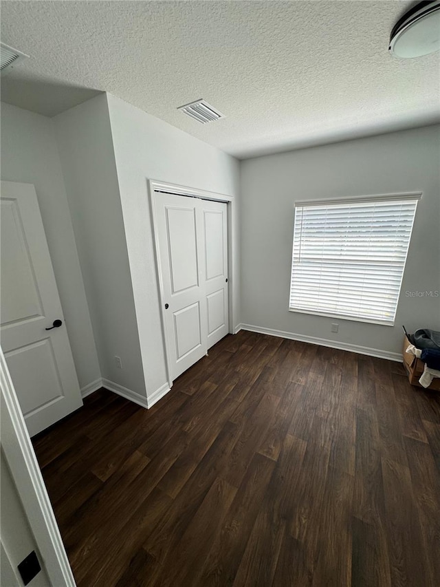 unfurnished bedroom featuring a textured ceiling, dark hardwood / wood-style flooring, and a closet