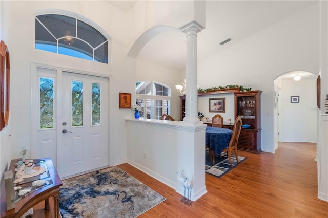 foyer entrance featuring light hardwood / wood-style flooring, a towering ceiling, and ornate columns