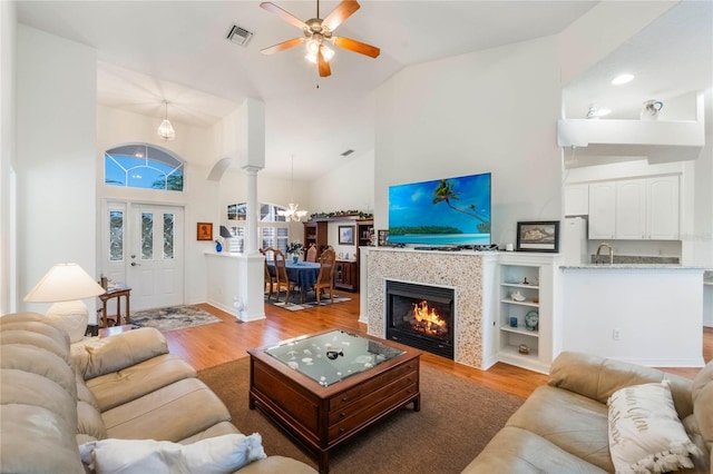 living room featuring ceiling fan with notable chandelier, ornate columns, sink, high vaulted ceiling, and light hardwood / wood-style flooring