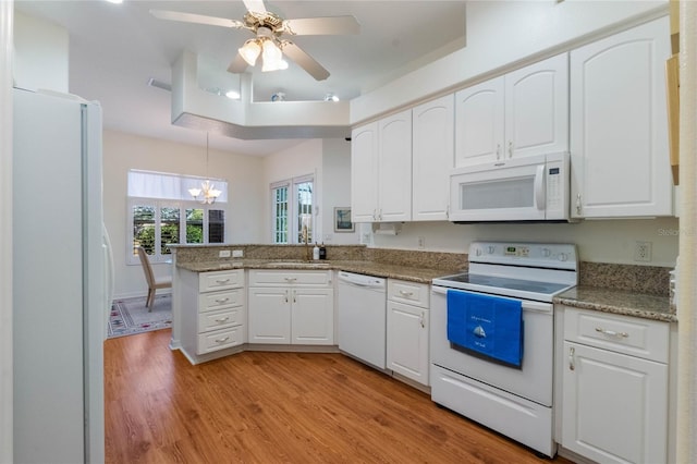 kitchen featuring white cabinets, kitchen peninsula, a tray ceiling, and white appliances