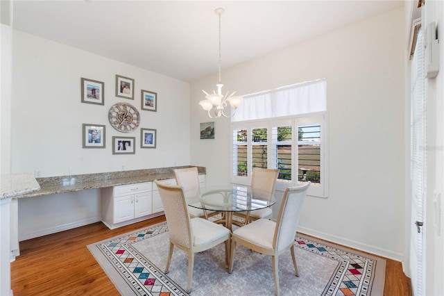 dining space with light wood-type flooring, built in desk, and a notable chandelier