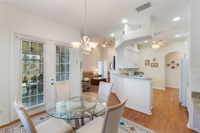 dining space with ceiling fan with notable chandelier, sink, and light hardwood / wood-style flooring