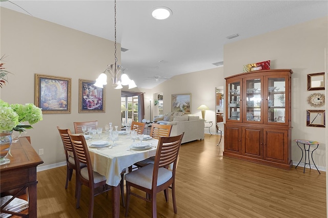 dining space featuring hardwood / wood-style floors, lofted ceiling, and an inviting chandelier