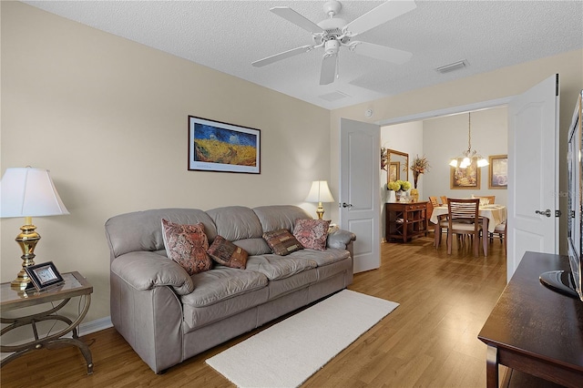 living room with hardwood / wood-style flooring, ceiling fan with notable chandelier, and a textured ceiling