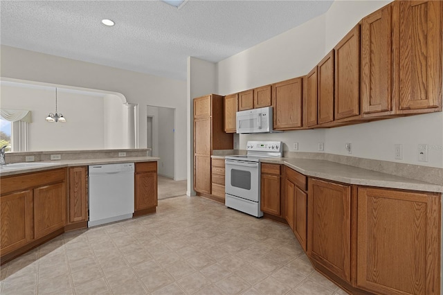 kitchen with sink, an inviting chandelier, hanging light fixtures, a textured ceiling, and white appliances