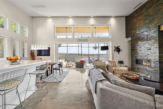 living room featuring a high ceiling, a wealth of natural light, a stone fireplace, and concrete floors