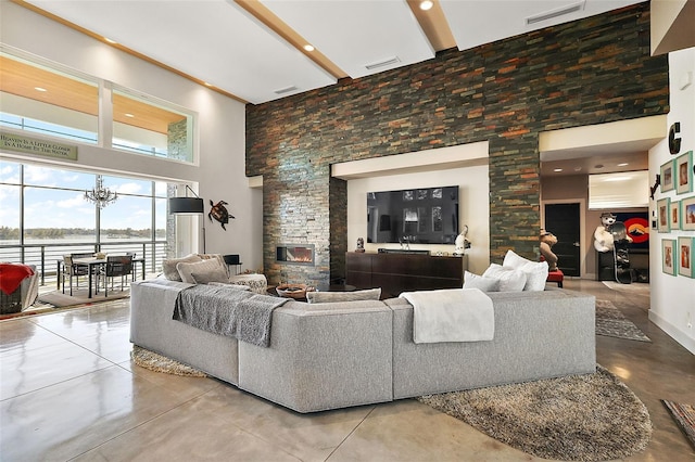 living room with concrete floors, a high ceiling, a stone fireplace, and an inviting chandelier