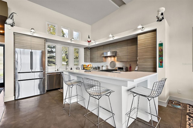 kitchen with range hood, stainless steel appliances, a towering ceiling, and a breakfast bar