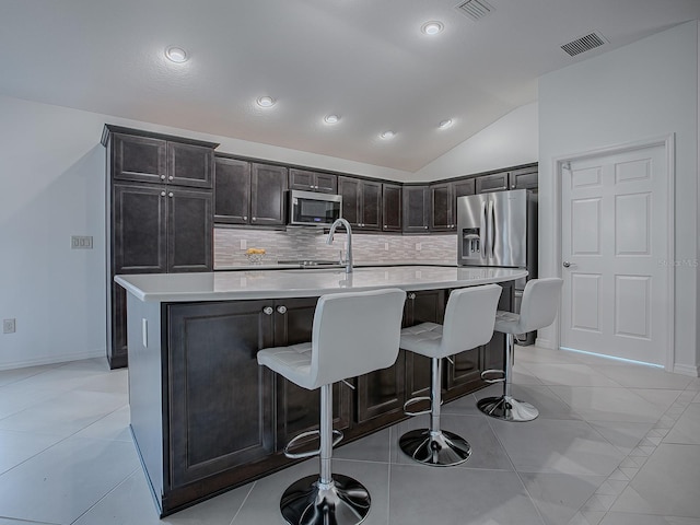 kitchen featuring light tile patterned flooring, appliances with stainless steel finishes, a kitchen island with sink, and lofted ceiling