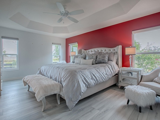 bedroom featuring ceiling fan, a tray ceiling, and multiple windows