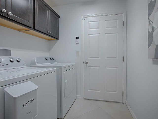 clothes washing area featuring cabinets, light tile patterned floors, and washer and clothes dryer