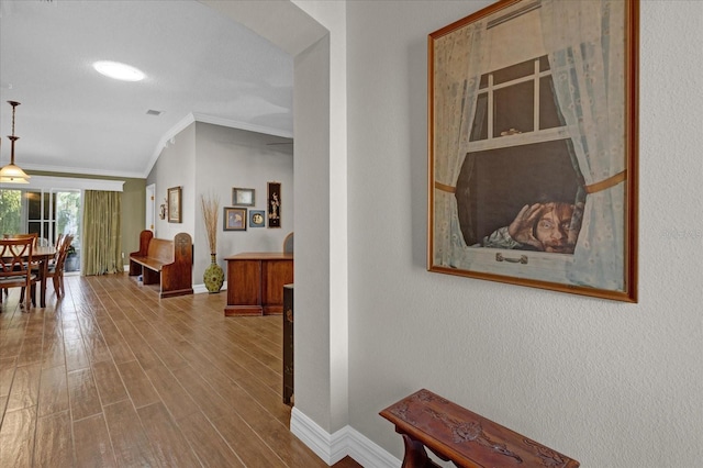 corridor featuring light wood-type flooring, crown molding, and vaulted ceiling