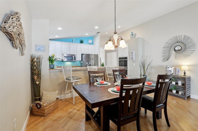 dining space with vaulted ceiling, an inviting chandelier, and light hardwood / wood-style flooring