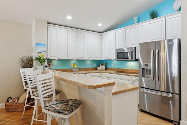 kitchen featuring a breakfast bar area, kitchen peninsula, stainless steel appliances, light hardwood / wood-style floors, and white cabinets