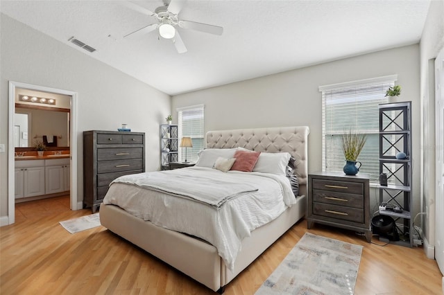 bedroom featuring vaulted ceiling, ensuite bath, light hardwood / wood-style floors, and multiple windows