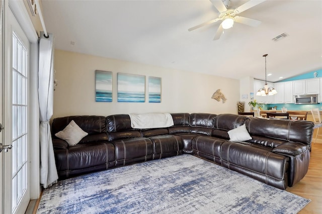 living room featuring lofted ceiling, ceiling fan with notable chandelier, and light wood-type flooring