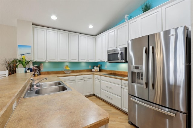 kitchen featuring appliances with stainless steel finishes, white cabinetry, sink, kitchen peninsula, and light hardwood / wood-style flooring