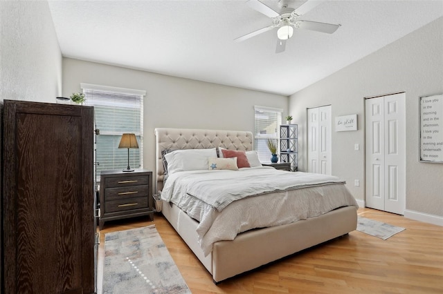 bedroom with ceiling fan, vaulted ceiling, light hardwood / wood-style floors, and multiple closets