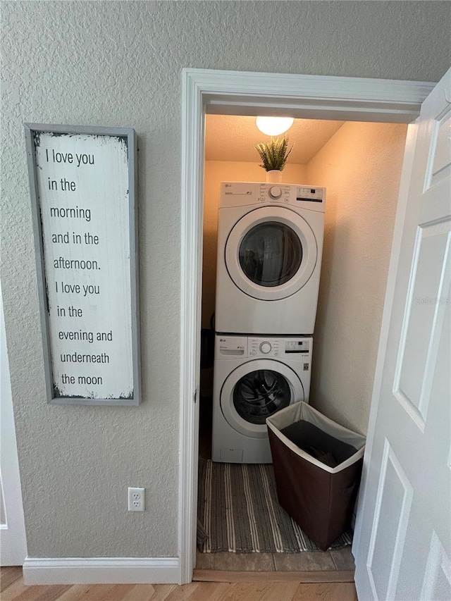 laundry room with wood-type flooring and stacked washer / drying machine