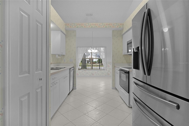 kitchen with white cabinets, hanging light fixtures, light tile patterned floors, stainless steel appliances, and an inviting chandelier