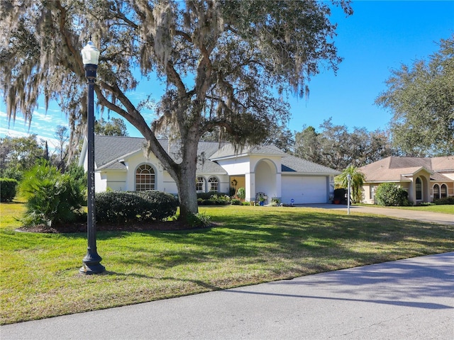 ranch-style home featuring concrete driveway, an attached garage, a front lawn, and stucco siding