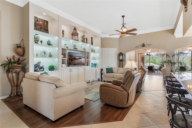 tiled living room with crown molding, ceiling fan, and built in shelves