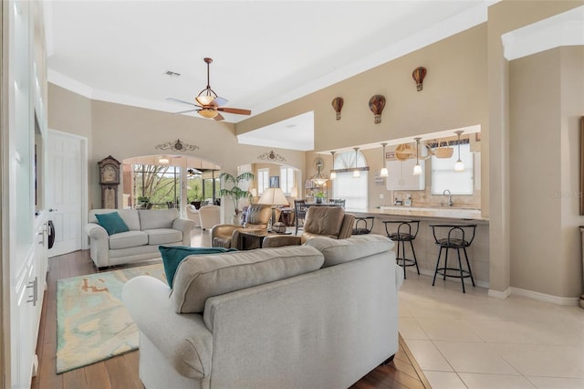 living room with crown molding, sink, light tile patterned flooring, and ceiling fan