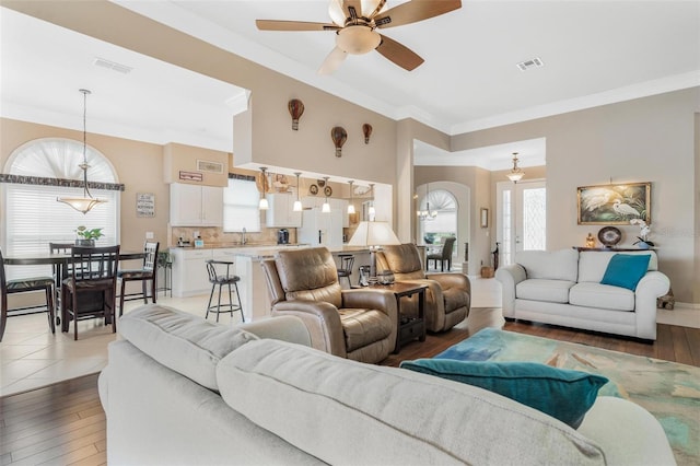 living room featuring hardwood / wood-style flooring, sink, crown molding, and ceiling fan with notable chandelier