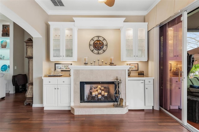 interior space featuring ornamental molding, dark hardwood / wood-style floors, a tile fireplace, and white cabinets