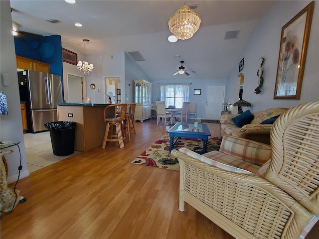 living room with lofted ceiling, ceiling fan with notable chandelier, and light wood-type flooring