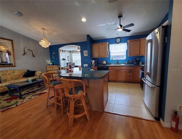 kitchen featuring sink, stainless steel fridge, hanging light fixtures, a kitchen breakfast bar, and a center island