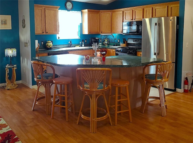 kitchen with sink, a center island, stainless steel fridge, range with gas stovetop, and light hardwood / wood-style floors