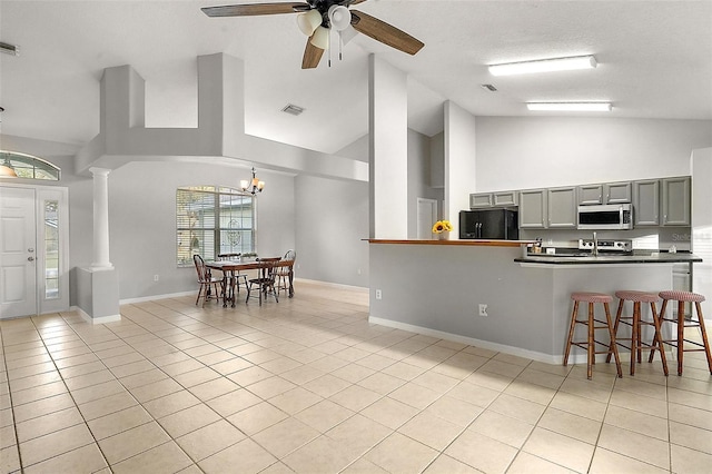 kitchen with appliances with stainless steel finishes, high vaulted ceiling, decorative columns, light tile patterned floors, and gray cabinetry