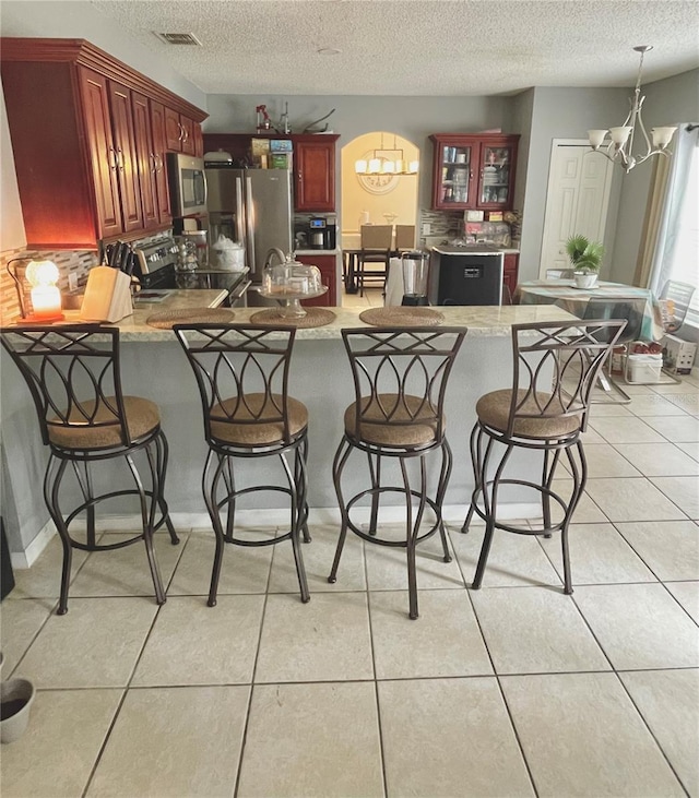 kitchen featuring kitchen peninsula, appliances with stainless steel finishes, a kitchen breakfast bar, and light tile patterned flooring