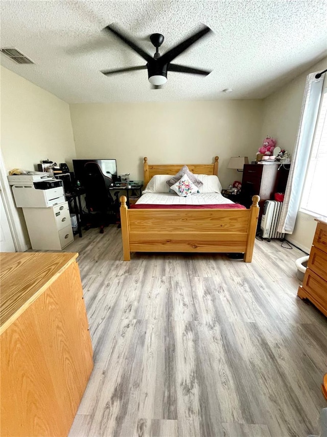 bedroom with a textured ceiling, ceiling fan, light hardwood / wood-style flooring, and radiator