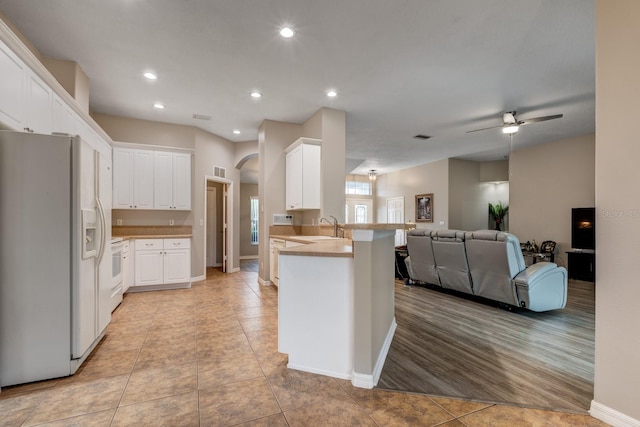 kitchen featuring kitchen peninsula, light tile patterned flooring, white cabinets, and white refrigerator with ice dispenser