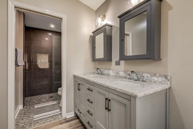 bathroom featuring hardwood / wood-style floors, tiled shower, toilet, and vanity