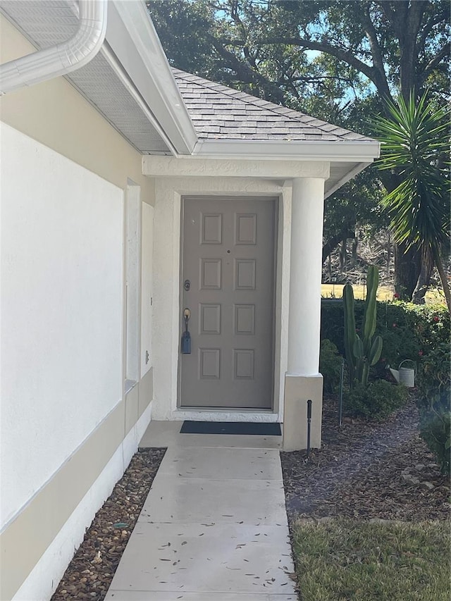 entrance to property featuring stucco siding and roof with shingles