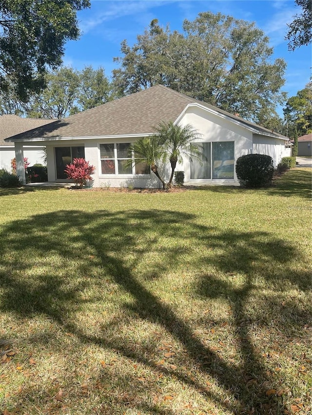 single story home with a shingled roof, a front yard, and stucco siding
