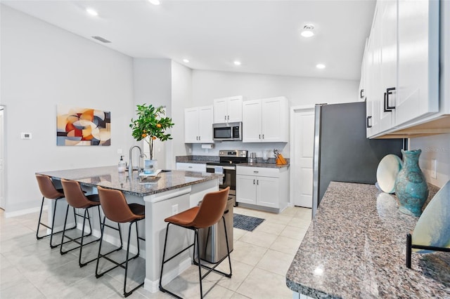 13557 Willow Bluestar Loop, Riverview, FL 33579 - kitchen featuring white cabinetry, dark stone countertops, a breakfast bar, light tile patterned flooring, and appliances with stainless steel finishes