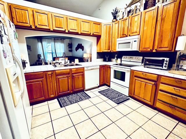 kitchen featuring tile countertops, light tile patterned floors, sink, and white appliances