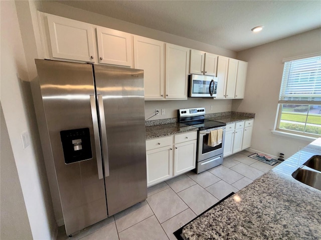 kitchen featuring stainless steel appliances, dark stone counters, white cabinets, and light tile patterned floors