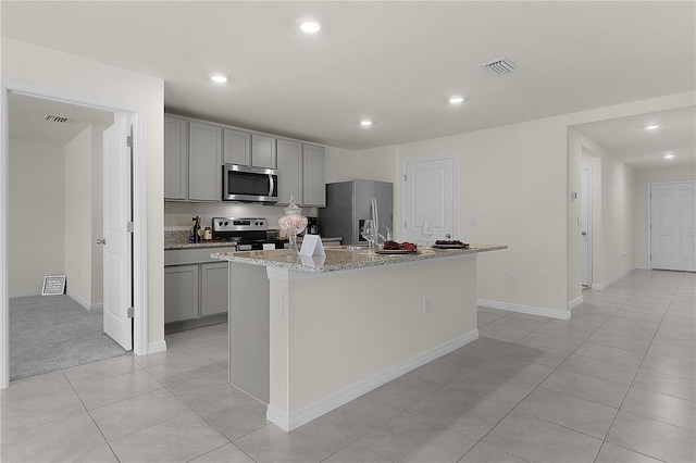 kitchen featuring gray cabinetry, light stone counters, a center island with sink, light tile patterned floors, and stainless steel appliances