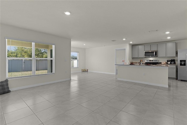 kitchen with light tile patterned flooring, light stone counters, a center island with sink, gray cabinets, and stainless steel appliances