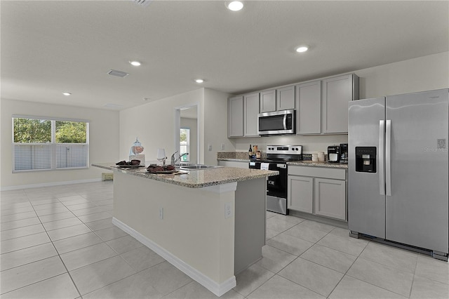 kitchen with sink, light tile patterned floors, gray cabinets, stainless steel appliances, and a kitchen island with sink