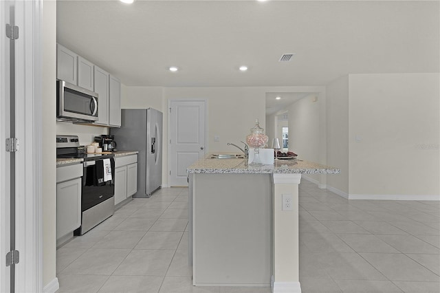 kitchen featuring sink, light tile patterned floors, an island with sink, stainless steel appliances, and light stone countertops