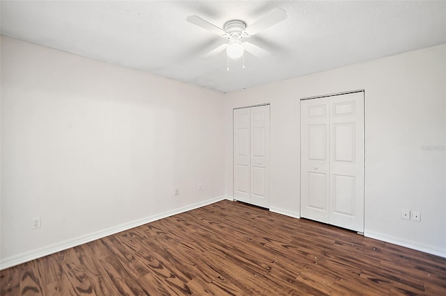 unfurnished bedroom with ceiling fan, multiple closets, and dark wood-type flooring